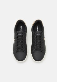 Zapatos sintéticos negros con cordones planos, detalles beige en el talón y suela de goma blanca. Presentan el logotipo de Levi's en la lengüeta.