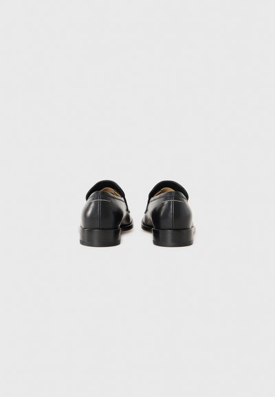 Chaussures noires en cuir avec une texture lisse, à bout arrondi et à petit talon. Avec des accents de couture le long de l'arrière et des côtés.