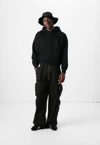 Sort hoodie med en frontlomme, parret med brede cargo bukser med flere lommer. Tilbehøret inkluderer en sort bucket hat.