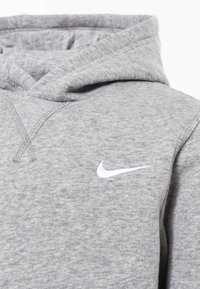 Svetle šedá mikina s kapucí s bílým vyšitým logem Nike swoosh na hrudi.