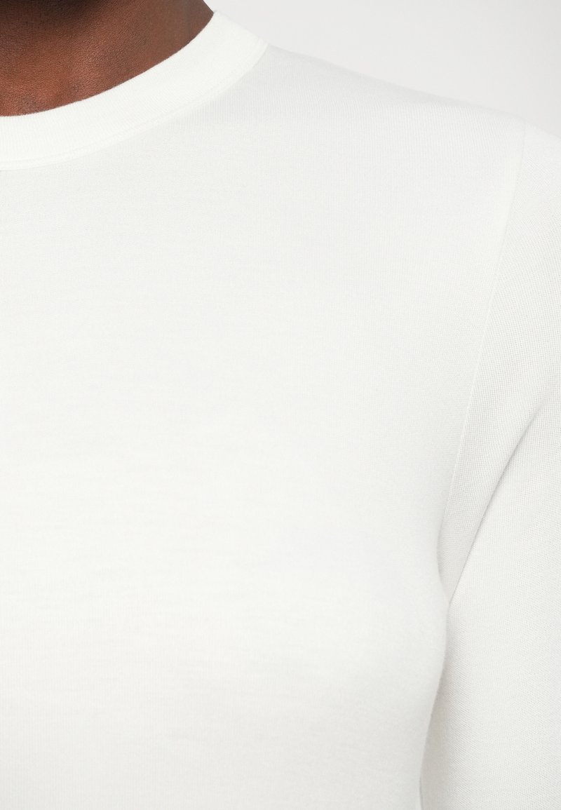 White cotton t-shirt with a round neckline and smooth texture, featuring long sleeves and a fitted design. No visible patterns or accents.