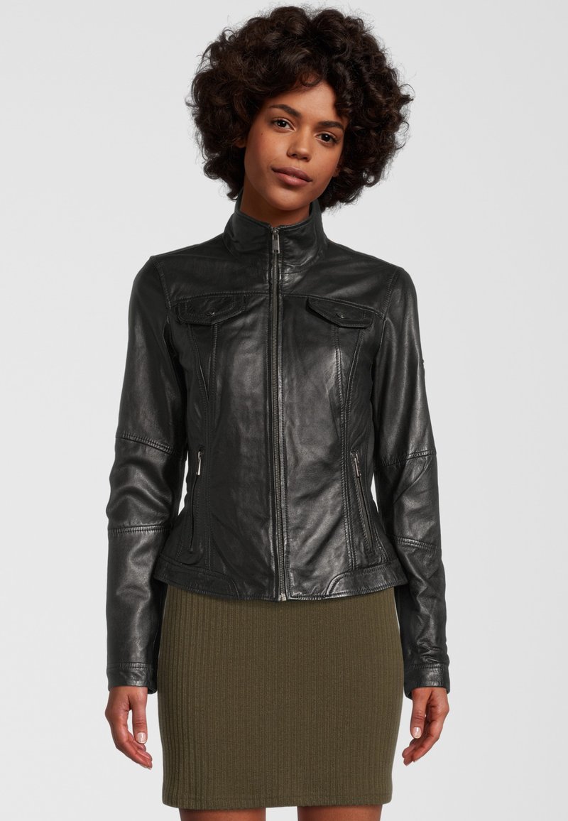 Zwarte leren jas met een hoge kraag, een getailleerd ontwerp, subtiele stikseldetails en twee voorkruisjes, gedragen over een geribde olijfgroene rok.