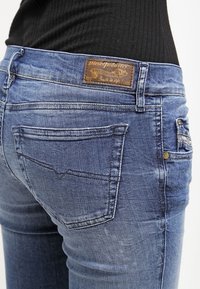 Figursydda blå denimjeans med en urblekt tvätt, utrustade med en brun läderplatta baktill, diskreta sömmar och standardfickor.