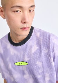 Violeta sieta ar caurumiem, ar melnu apkakli un zaļu Nike logo. Audums ir ar punktveida rakstu un mākoņveida dizainu.