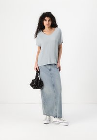 Lys grå kortærmet top med V-udskæring, kombineret med en lang denimnederdel. Outfitet fuldendes med hvide sneakers og en sort mønstret taske.