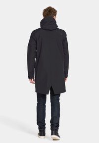 Sort lang jakke med hætte, der har et slankt design og en længere rygkant. Materialet ser let og glat ud, med minimale detaljer.