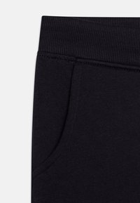 Mørk marineblå joggebukser med ribbestrikket liv, sidelomme og glatt stoffstruktur. Har ren søm og et enkelt design.