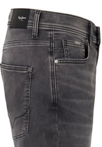 Vaqueros de mezclilla gris con un corte ajustado, presentando un parche de cuero negro con el logotipo, diseño de cinco bolsillos y costuras en contraste en los bolsillos traseros.