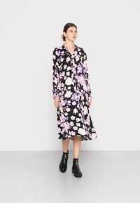 Vestido preto floral com padrões de flores roxas e pink, mangas longas, frente com botões e uma saia fluida de comprimento médio. Botas pretas até ao tornozelo.