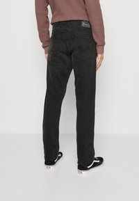 Jeans neri in denim con un design a gamba dritta, dotati di due tasche posteriori e di un'etichetta visibile sulla cintura. Abbinati a scarpe nere.