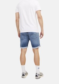 Vaaleansiniset farkkushortsit, joissa on käärityt lahkeet ja takataskut ommelkoristeilla. Yhdistetty yksinkertaiseen valkoiseen t-paitaan ja lenkkareihin.