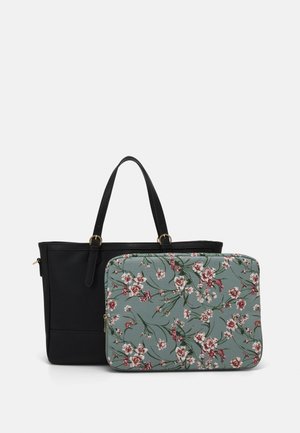 Sac cabas en cuir noir avec deux poignées à côté d'une housse d'ordinateur portable zippée verte avec un motif floral rose.