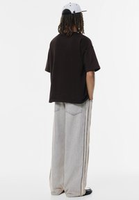 Brązowy, oversize t-shirt, szerokie jasnoszare dżinsy z bocznymi paskami i szara czapka. Casualowy strój o luźnym kroju i minimalnych detalach.