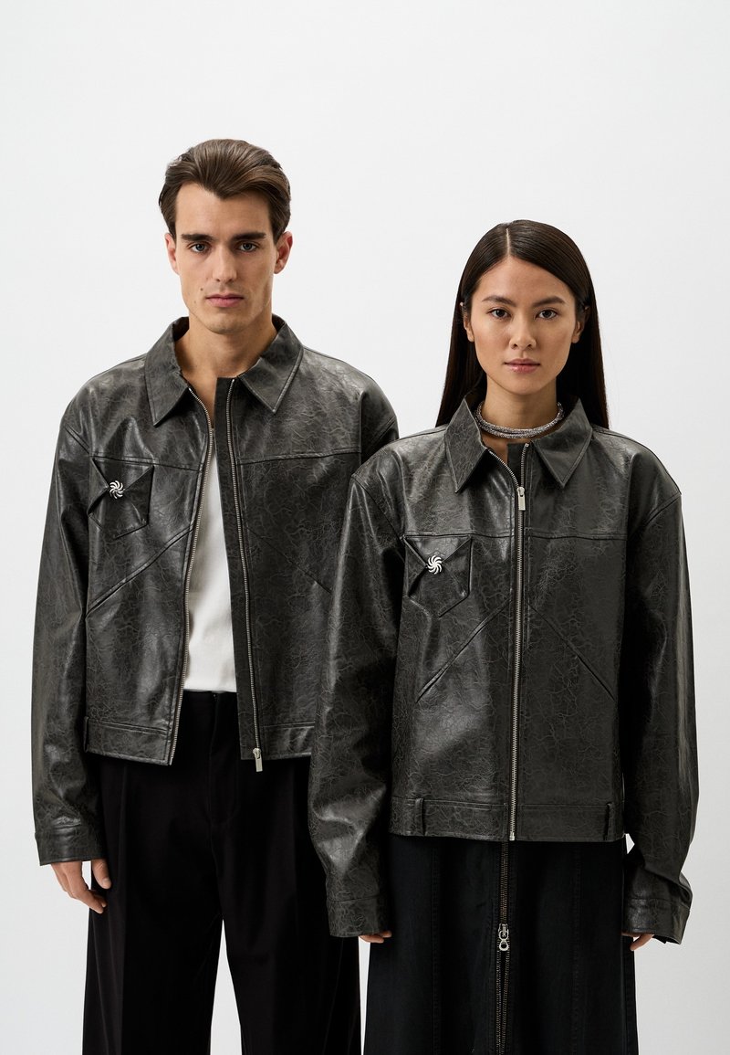 Schwarze Lederjacken mit strukturiertem Finish, mit Reißverschluss, spitzen Kragen und Details an den Fronttaschen. Getragen von zwei Personen.