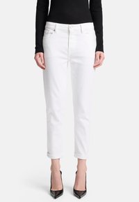 Jeans in denim bianco con taglio dritto, risvolti e tasche frontali, abbinati a scarpe nere con tacco alto e un top aderente nero.