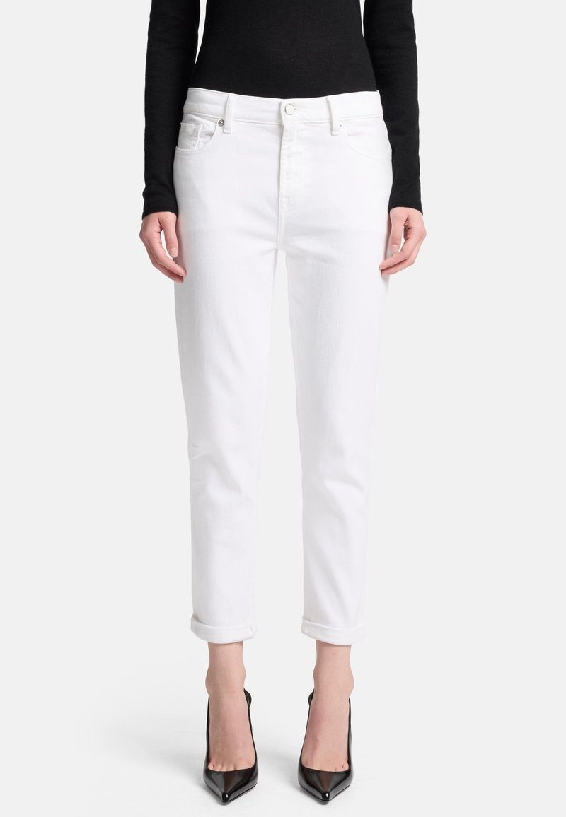 Weiße Jeans aus Denim mit geradem Schnitt, aufgerollten Säumen und Fronttaschen, kombiniert mit schwarzen High-Heels und einem eng anliegenden schwarzen Oberteil.