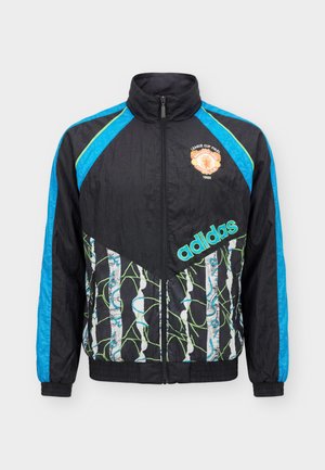 Musta Adidas vetoketjutakki, jossa sinisiä raidoituksia olkapäillä ja hihoissa, abstrakteja vihreitä ja valkoisia kuvioita, sekä Manchester Unitedin 1992 liigacupin merkki.