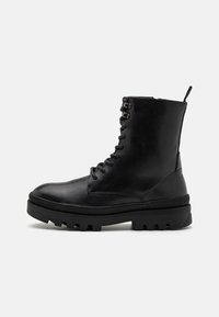 Botas de tobillo de cuero negro con puntera redondeada, parte delantera con cordones y suela de goma gruesa con acentos estriados.