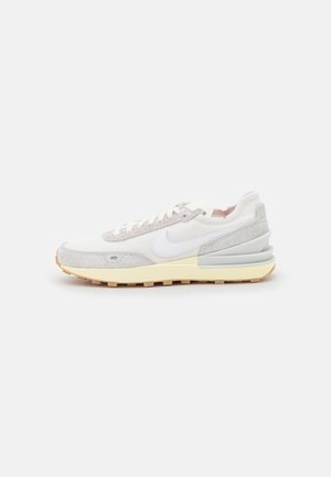 Biała i jasnoszara tenisówka Nike z kremową podeszwą i teksturowaną cholewką, pokazana w profilu bocznym na jednolitym jasnym tle.