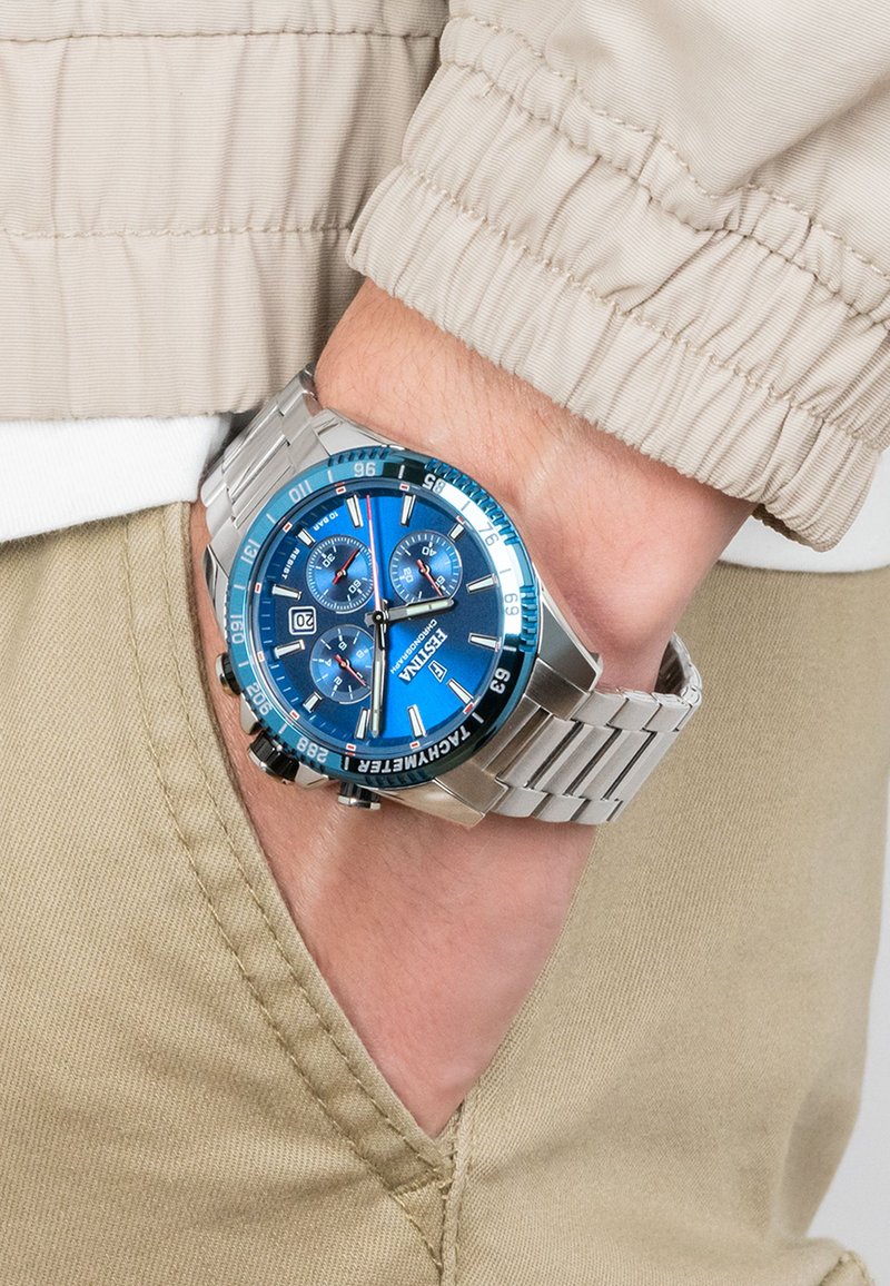 Montre en acier inoxydable argenté avec un cadran bleu, trois sous-cadrans et un affichage de la date. Dotée d'un bracelet à maillons et d'une lunette noire avec des accents bleus.