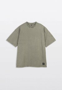 Oliwkowa koszulka z krótkim rękawem wykonana z bawełny. Posiada okrągły dekolt, charakterystyczne szwy oraz małą naszywkę z logo na dolnym brzegu.