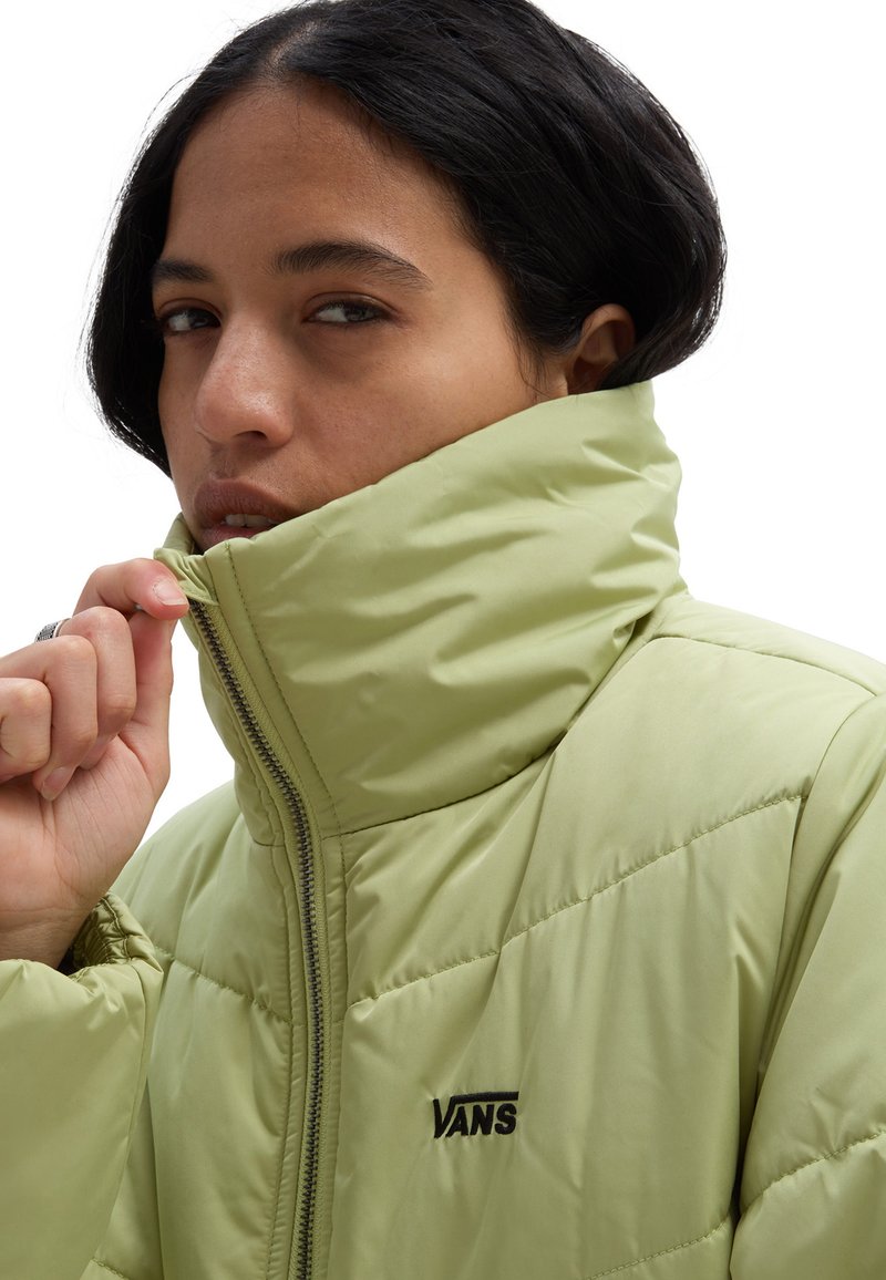 Jasnozielona puchowa kurtka z wysokim kołnierzem i zapięciem na zamek, z subtelnymi przeszyciami i czarnym akcentem logo z przodu.