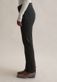 Jeans droits noirs en denim. Présentent une taille haute, deux poches arrière, et sont associés à des bottes à talons marron, le tout sur un fond neutre.