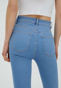 Jeans de mezclilla de tiro alto en un tono azul claro, con una textura suave, diseño de cinco bolsillos y detalles de costura sutiles en los bolsillos traseros.