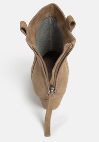 Bottine en daim marron avec un bout rond, double zips sur les côtés et languettes pour tirer. Doublée de tissu gris, avec une texture douce.