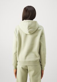 Sweatshirt verde claro feito de tecido macio, apresentando um bolso canguru, punhos canelados e capuz com cordão. Design simples sem gráficos.