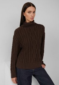 Brauner Rippstrick-Turtleneck-Pullover mit strukturiertem Muster, geripptem Saum und Bündchen. Kombiniert mit dunkelblauen Jeanshosen.