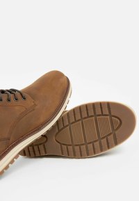 Bruine leren boots met een ronde neus, voorzien van zwarte veters, een contrasterende witte zool en een gestructureerde rubberen zool voor grip.