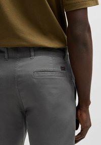 I pantaloni di cotone grigi presentano un design aderente con una tasca posteriore singola e un'etichetta con logo. Il materiale ha una texture liscia.