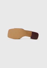 Zapato de tacón alto con parte superior burdeos, punta cuadrada y tacón cuadrado ancho. La suela es de color beige con una textura estriada para mayor agarre. Diseño minimalista.