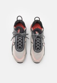 Grå sportskor med en strukturerad mesh-överkappa, svarta och röda detaljer samt grå snören. Har en dragtab för enkel påtagning.