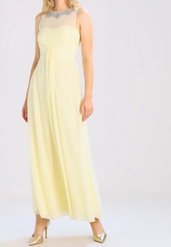 Robe jaune longue jusqu'au sol avec un décolleté transparent, une taille froncée et des embellissements argentés. Associée à des chaussures à talons hauts dorées.