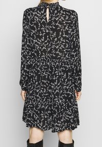 Robe noire à manches longues, motif floral blanc, détail dos en trou de serrure, taille froncée ; fabriquée en tissu léger.