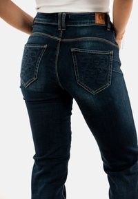 Jeans in denim blu scuro con vita alta, due tasche posteriori con loghi impresso e cuciture a contrasto.