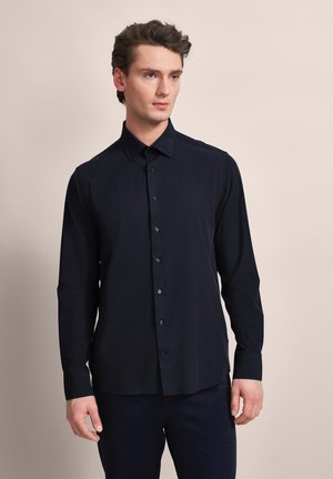 Marineblaue Langarmhemd mit Knopfleiste, klassischem Kragen, glatter Textur und schwarzen Knöpfen, getragen mit dunklen Hosen.