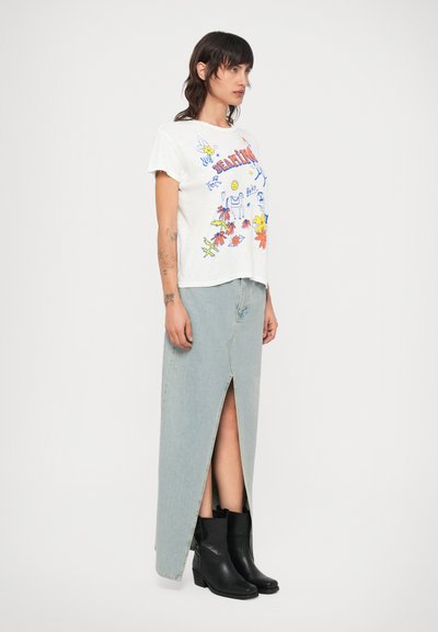 Tricou alb cu un design grafic colorat de flori și soare, asortat cu o fustă maxi din denim de culoare bleu deschis, cu o deschidere frontală, și cizme negre până la gleznă.