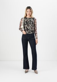 Haut transparent à manches longues avec un imprimé animal marron et gris, associé à un jean évasé bleu foncé à taille haute et couture contrastante.