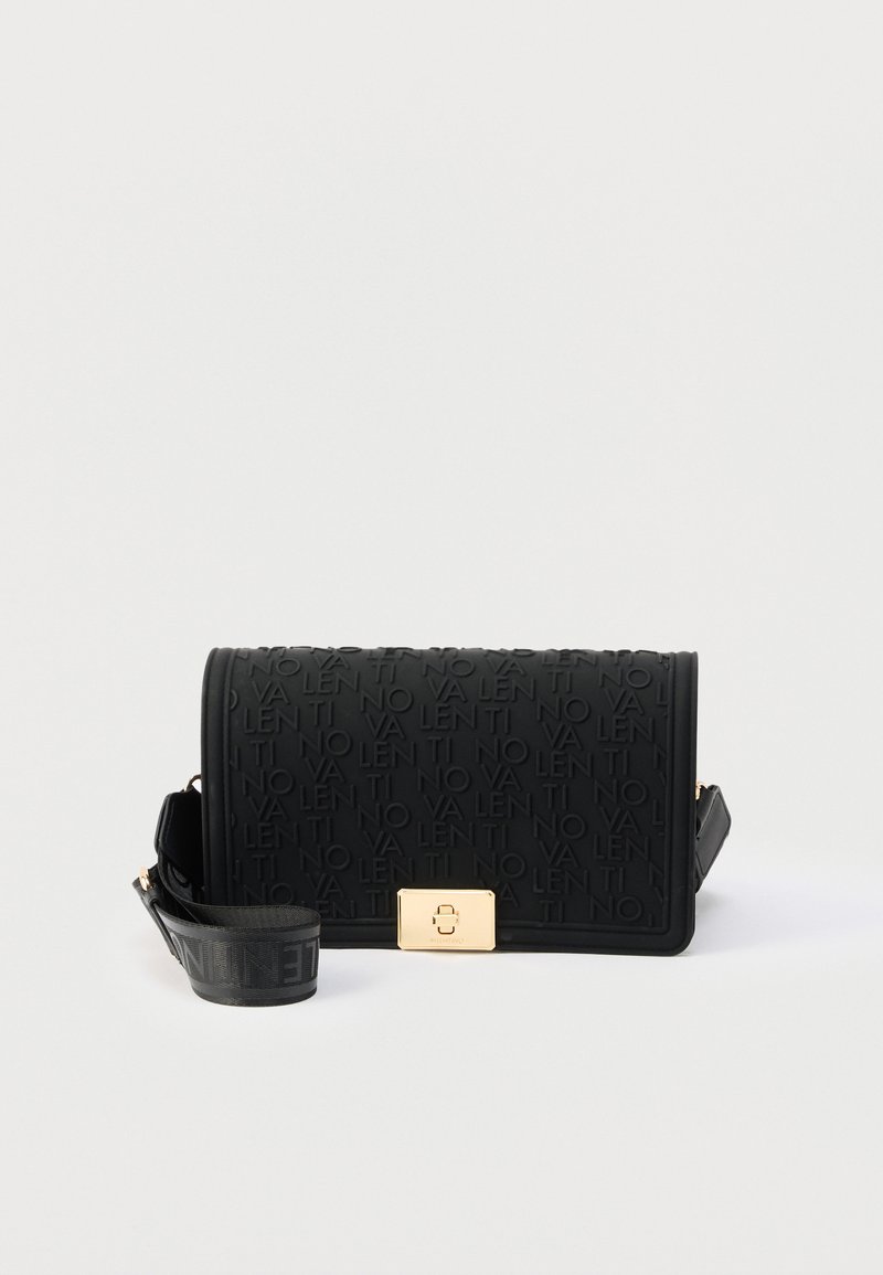 Μαύρη ορθογώνια τσάντα ώμου με ανάγλυφο επαναλαμβανόμενο κείμενο, χρυσό κούμπωμα και ρυθμιζόμενο λουρί τυλιγμένο δίπλα της σε λευκό φόντο.