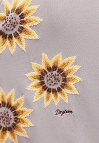 Trois motifs de tournesol brodés avec des pétales jaunes et marron sur un tissu gris.