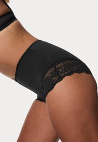 Mutandine nere a vita alta con tessuto liscio e bordo in pizzo con motivi floreali lungo i bordi. Accentuate da dettagli a ondine.