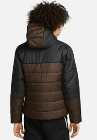 Giacca imbottita con una combinazione di colori nera e marrone, caratterizzata da un cappuccio, una texture trapuntata e un design aderente.