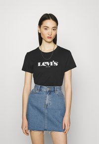 Musta puuvillainen t-paita, jossa on valkoinen "Levi's" -logo, yhdistettynä siniseen farkku mini-hameeseen, jossa on revitty helma ja korkeavyötäröinen muotoilu.
