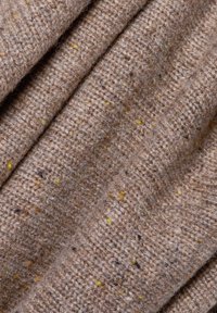 Textil mit Struktur in Beige, das gelbe und braune Sprenkel aufweist. Das Material wirkt weich mit einem gestrickten Muster und subtilen Farbvariationen.