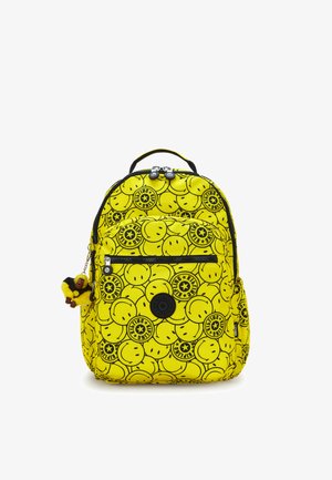 Mochila de color amarillo brillante con cara sonriente negra y logotipos de estrellas, bolsillo delantero con cremallera y un pequeño llavero de mono de peluche adjunto.