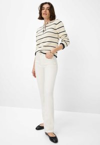 Gebreide trui in crème met marineblauwe strepen en een kraag met drie knopen, gecombineerd met witte flare jeans en zwarte ballerina's.