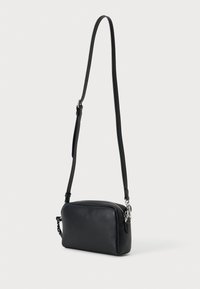 Černá kožená crossbody taška s obdélníkovým tvarem, nastavitelným popruhem, uzavíráním na zip a malým vzorovaným akcentem na popruhu.